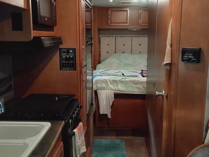 Cozy RV rental interior: kitchenette with sink, stove, microwave, leading to a bedroom with a bed and wood cabinets.. Winnebago Minnie Winnie 2016