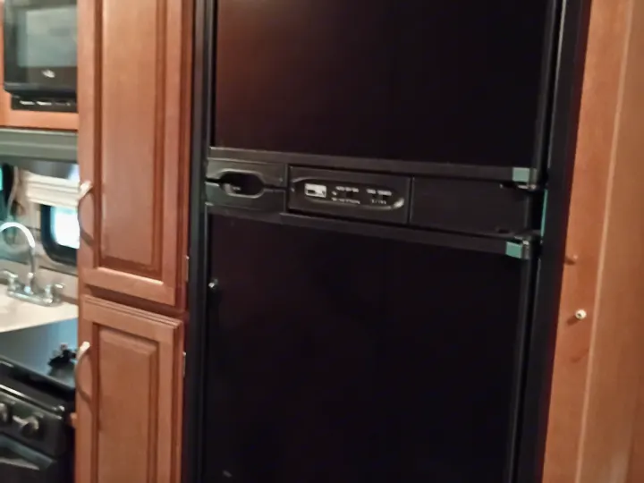 Inside an rv rental: a black two-door refrigerator, surrounded by wood cabinets, with a microwave and sink visible.. Winnebago Minnie Winnie 2016