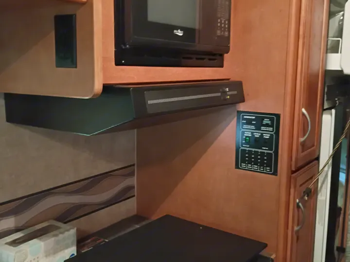 RV rental interior: compact kitchen with microwave, range hood, and a control panel for generator, water heater, and tank levels.. Winnebago Minnie Winnie 2016