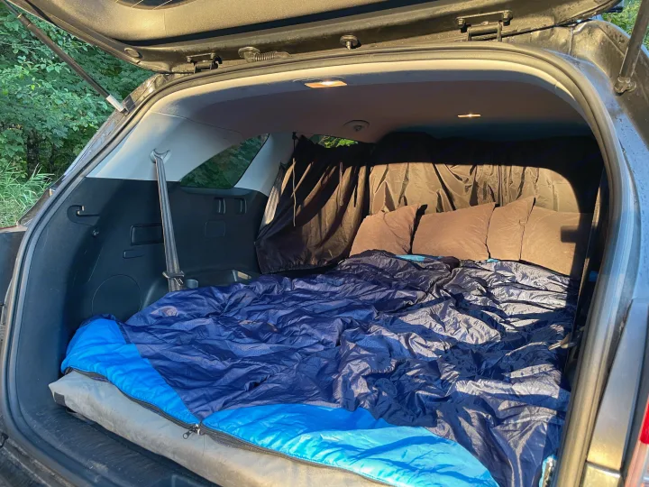 Cozy car camping setup in an SUV, featuring a sleeping bag, pillows, and privacy curtains. A great alternative to an rv rental.. KIA Sorento 4X4 2017