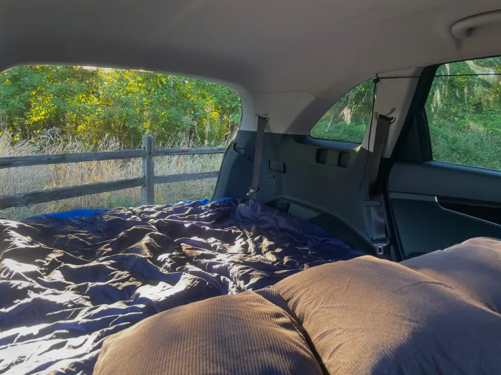 Inside an RV rental: a snug car camping setup with a sleeping bag & pillow, overlooking a sunny nature scene. Road trip vibes!. KIA Sorento 4X4 2017