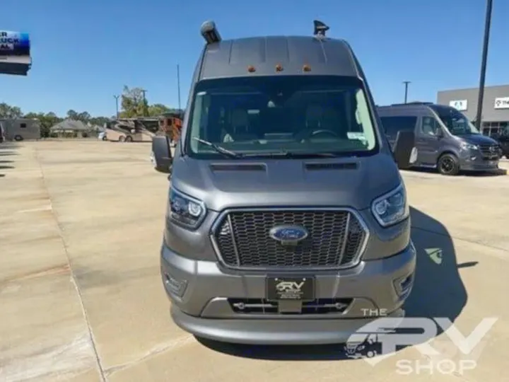 Custom grey Ford Transit camper van with a snorkel, perfect for rv rental. Seen at an RV shop with other vehicles.. Midwest Automotive Designs Passage 2024
