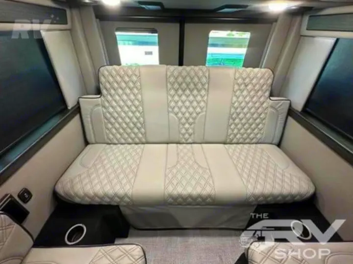 Inside this luxurious rv rental, a light-colored quilted bench seat converts to a bed, flanked by windows and additional seating.. Midwest Automotive Designs Passage 2024