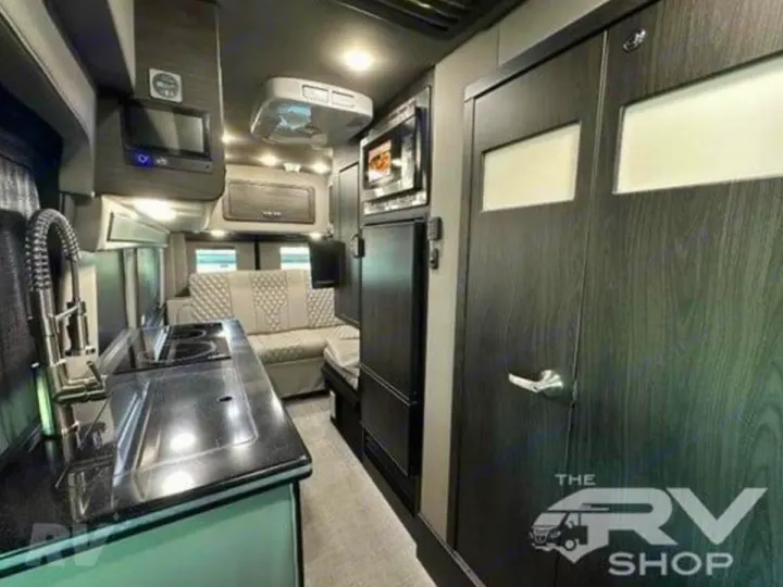 Inside a compact RV rental, showing a modern kitchen, rear seating, and dark wood-grain storage doors for an efficient living space.. Midwest Automotive Designs Passage 2024
