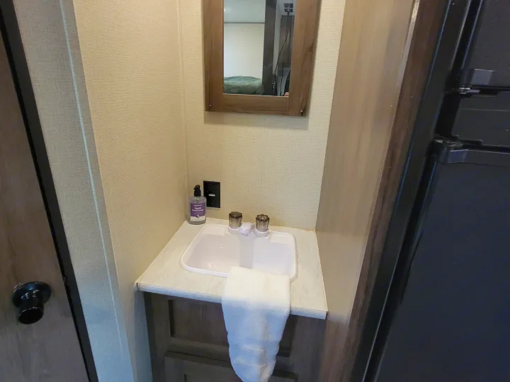 Practical rv rental bathroom vanity with a compact sink, mirror reflecting a bed, hand soap, and towel. Ready for your trip.. Forest River Avenger 2020