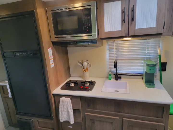 Compact RV rental kitchen featuring a fridge, microwave, stove, sink, and Keurig coffee maker, ready for your adventures.. Forest River Avenger 2020