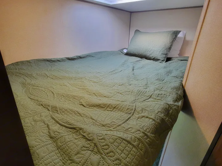 Cozy RV rental bunk bed with an olive green quilted comforter and pillow, offering a comfortable sleeping space.. Forest River Avenger 2020