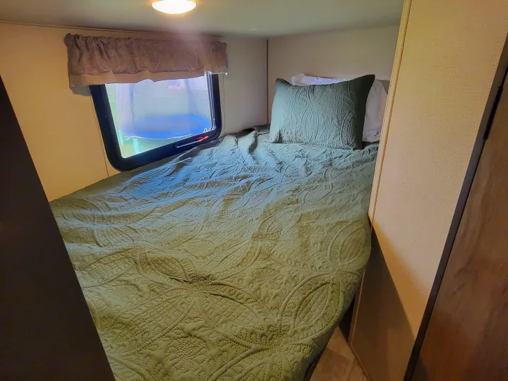 Cozy RV rental bedroom with a green quilted bed, pillow, and window showing a blue pool outside.. Forest River Avenger 2020