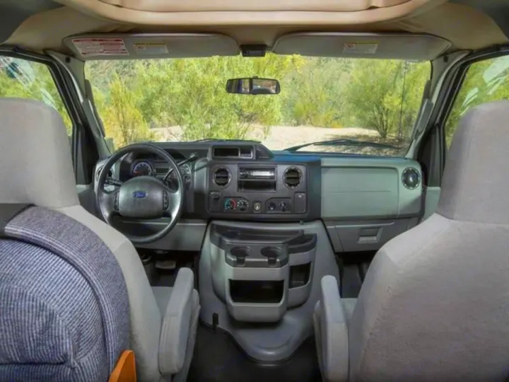 Inside an RV rental, the spacious front cabin shows the dashboard with steering wheel, controls, and two gray seats for your travels.. Thor Majestic 2023