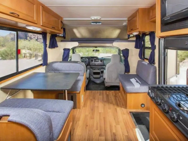 Inside an rv rental: full kitchen, dinette, overhead bed, and bright windows, with wood floors, ready for travel.. Thor Majestic 2023