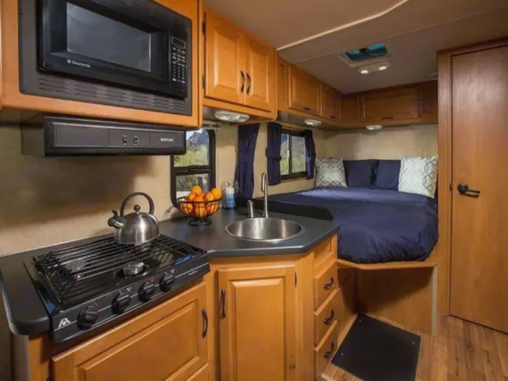 Compact rv rental interior showcasing a kitchen with stove, microwave, sink, and a cozy bedroom with blue bedding.. Thor Majestic 2023
