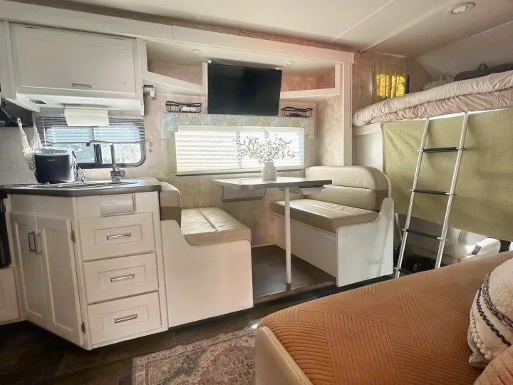 Modern rv rental interior showing a kitchenette, dinette with TV, and bunk beds with a ladder, providing compact living space.. Winnebago Minnie Winnie 2018