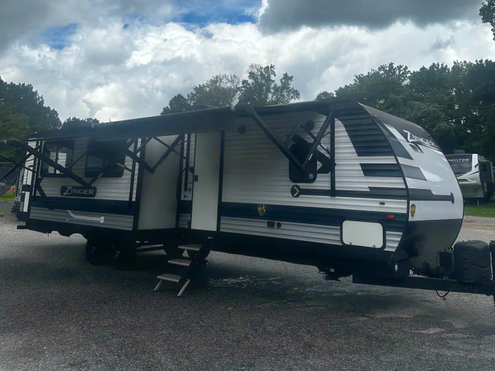 A Zinger travel trailer RV rental, with its awning out, parked on gravel under a dramatic cloudy sky.. Crossroads RV Zinger 2020