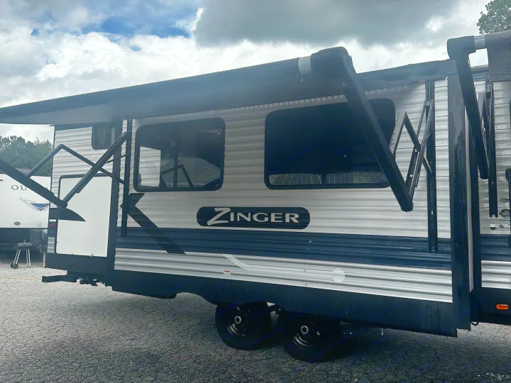 A Zinger RV rental travel trailer with an extended black awning, parked on gravel under a cloudy sky.. Crossroads RV Zinger 2020