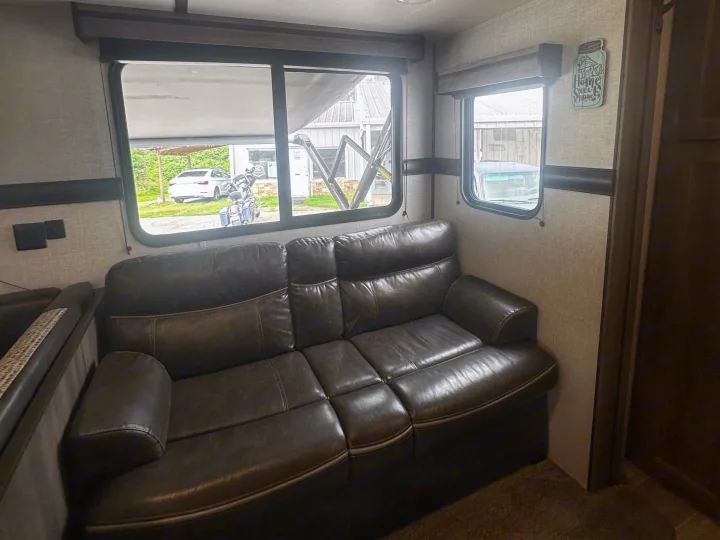 Cozy rv rental interior showcasing a brown leather sofa, large windows with outside views, and overhead blue LED lighting.. Crossroads RV Zinger 2020