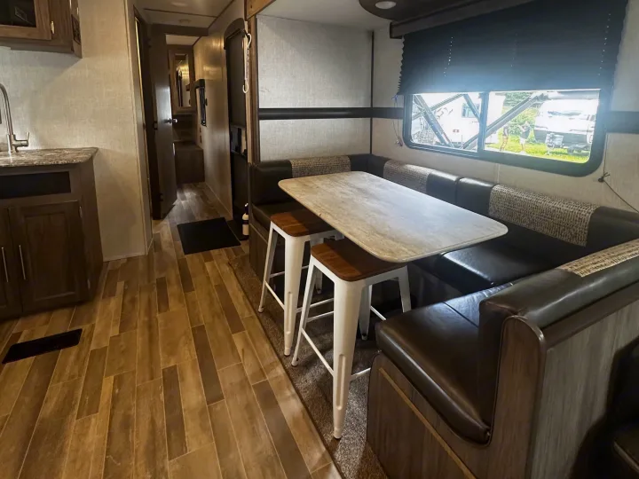 Spacious RV rental interior featuring a cozy dining area with table and booth seating, plus a peek into the kitchen and hallway.. Crossroads RV Zinger 2020