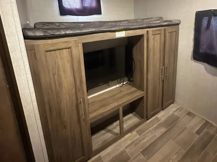RV rental interior: bunk beds over a TV entertainment unit with storage, featuring a ceiling AC unit and wood-look plank flooring.. Crossroads RV Zinger 2020