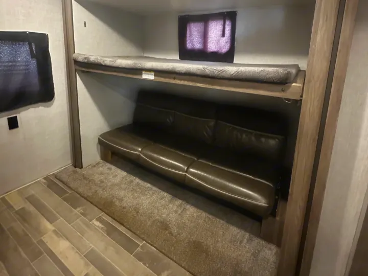 RV rental interior featuring bunk beds: an upper bed with a grey mattress and a lower brown sofa, on wood-look flooring.. Crossroads RV Zinger 2020