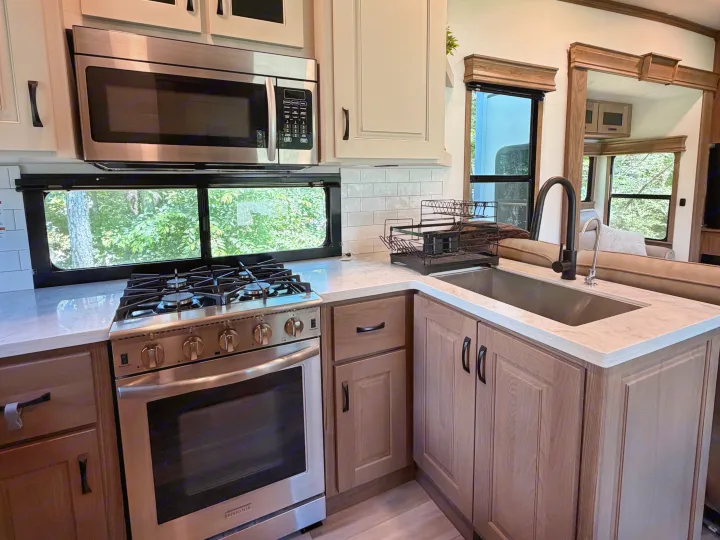A bright RV rental kitchen: modern stainless steel appliances, white marble counters, and nature views from the window.. Alliance RV Paradigm 2024