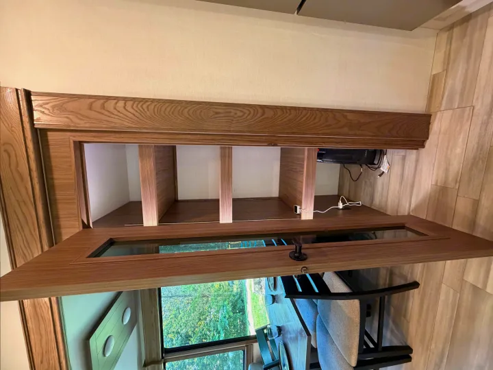 RV rental: Open wooden overhead cabinet with shelving, USB chargers, overlooking the interior dining area and lush outdoor view.. Alliance RV Paradigm 2024