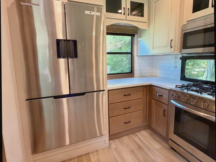 Modern RV rental kitchen with stainless steel appliances: fridge, oven, microwave, white subway tile, and wood cabinets.. Alliance RV Paradigm 2024