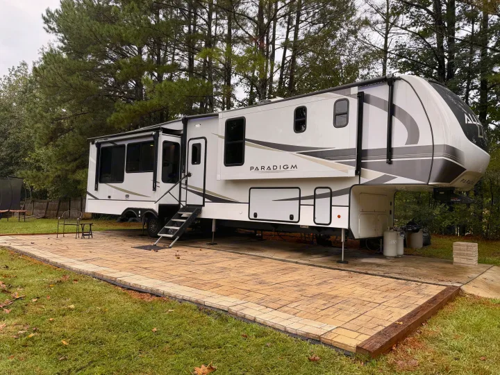 Luxury Paradigm fifth-wheel RV setup on a paved site, ready for a comfortable rv rental experience amidst pine trees.. Alliance RV Paradigm 2024