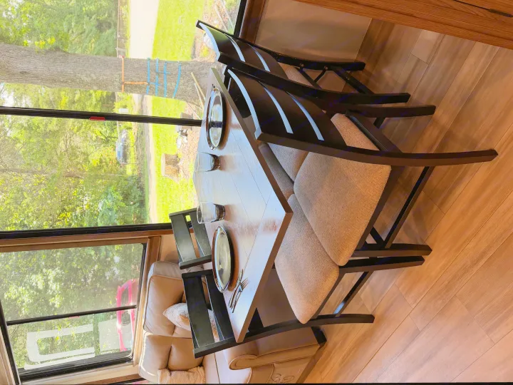 RV rental dining area with wooden table, chairs, and a scenic window view of a tree, grass, and a parked car outside.. Alliance RV Paradigm 2024