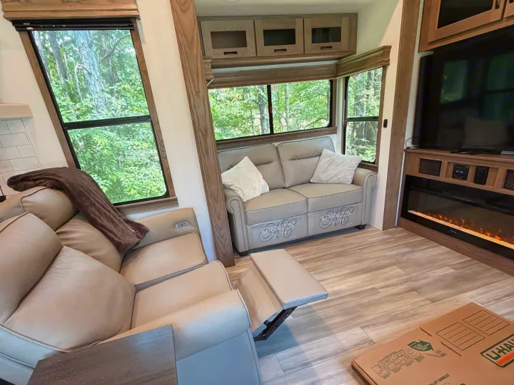 Cozy RV rental interior with forest views, recliners, fireplace, and "Kensington Collection" sofas.. Alliance RV Paradigm 2024