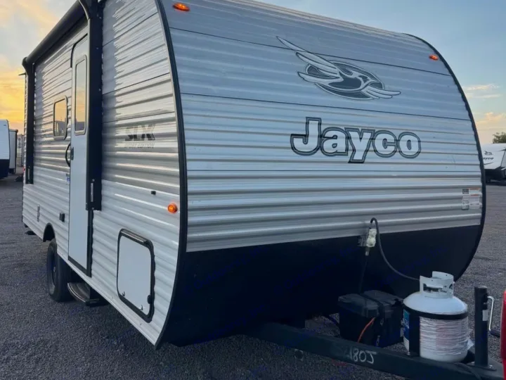 Ready for adventure! This gray Jayco travel trailer, seen parked outdoors, is ideal for an rv rental, featuring propane tanks & an awning.. Jayco Jay Flight 2025