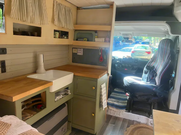 This RV rental features a custom camper van kitchenette: wood counters, green cabinets, organized storage, and a view into the front cabin.. Dodge Promaster 2500 high roof 2019