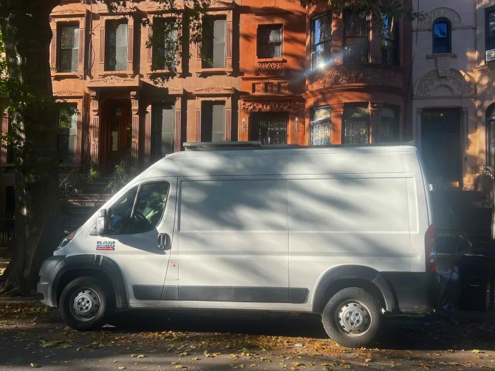 White Ram ProMaster van, possibly an rv rental, on a street with brownstone buildings. Sunlit scene with tree shadows & autumn leaves.. Dodge Promaster 2500 high roof 2019