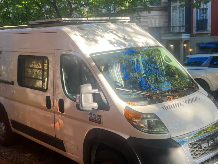 White Ram Promaster 2500 campervan, an RV rental, with roof-mounted solar panels, parked on a sunny street.. Dodge Promaster 2500 high roof 2019