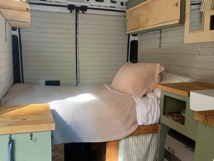 Bright RV rental interior featuring a cozy bed, built-in kitchen area with a sink, and a VEVOR cooler for mobile living.. Dodge Promaster 2500 high roof 2019