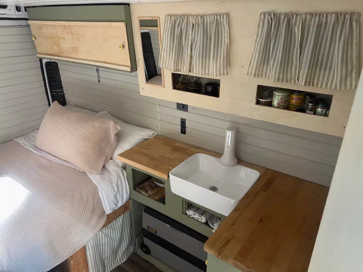 RV rental interior showcases a cozy bed, compact kitchen with sink, wooden counters, smart storage, and a portable fridge.. Dodge Promaster 2500 high roof 2019