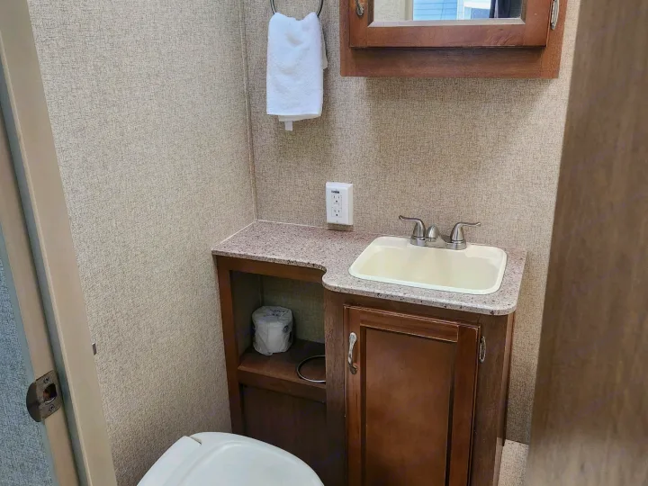 Explore this functional RV rental bathroom, featuring a partially visible toilet, compact sink vanity, medicine cabinet, and towel.. Coachmen Catalina 293qbck 2015