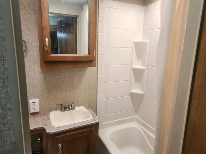 This RV rental bathroom features a vanity with a sink, medicine cabinet, and shower/tub combo. Compact & functional.. Coachmen Catalina 293qbck 2015