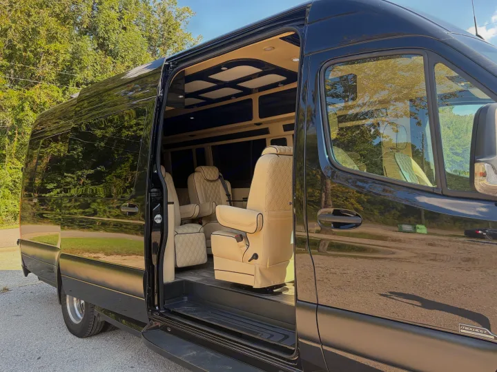 This black luxury conversion van rv rental, with its side door open, reveals a plush cream interior and captain's chairs.. Midwest Automotive Designs Luxe Cruiser 2025