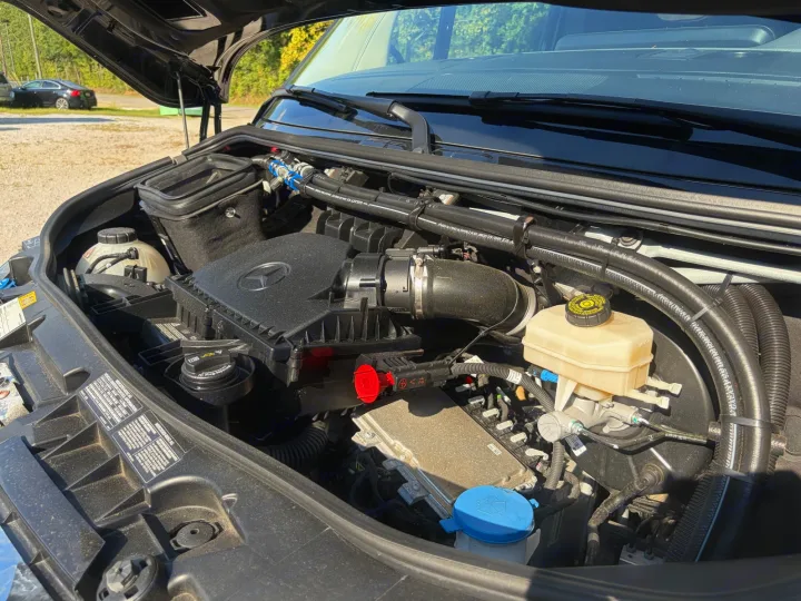 Mercedes-Benz Sprinter van engine bay for RV rental. Shows engine, air filter, brake fluid, and coolant reservoir under open hood.. Midwest Automotive Designs Luxe Cruiser 2025