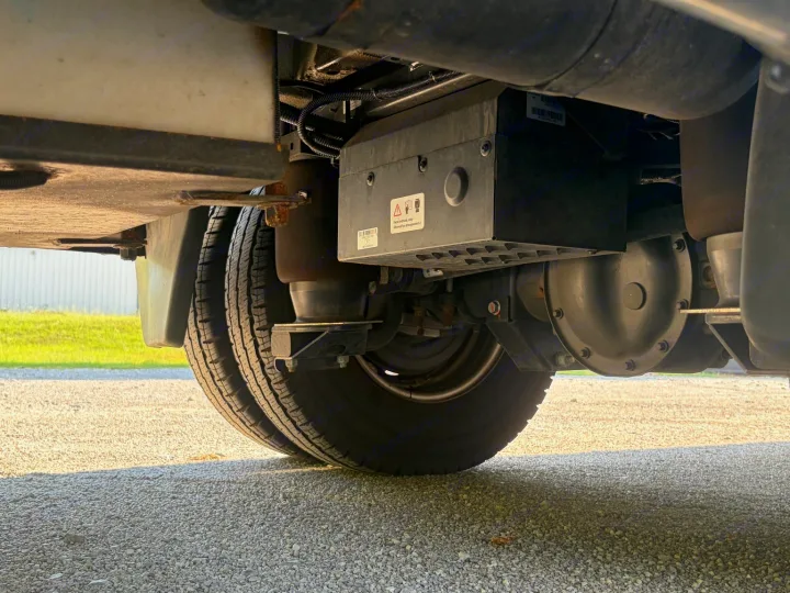 Undercarriage view of an RV rental, featuring dual rear tires, air suspension, differential, and utility box. Gravel ground.. Midwest Automotive Designs Luxe Cruiser 2025