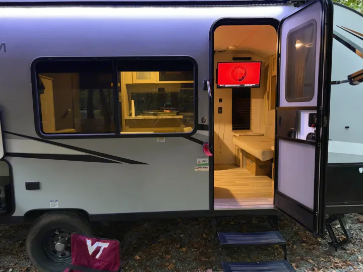 This rv rental travel trailer, with its open door revealing a cozy TV/kitchen interior, is set for camping.. Forest River Wildwood FSX Platinum 2023