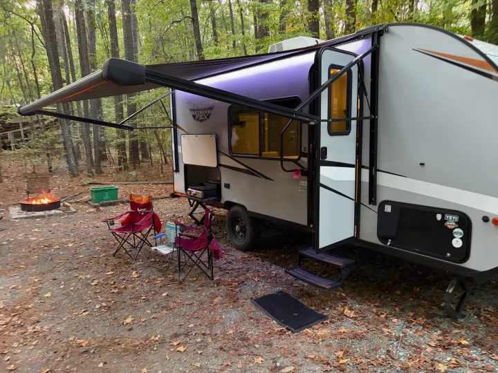 RV rental setup at dusk, featuring a Wildwood FSX travel trailer with an extended awning, campfire, and chairs.. Forest River Wildwood FSX Platinum 2023