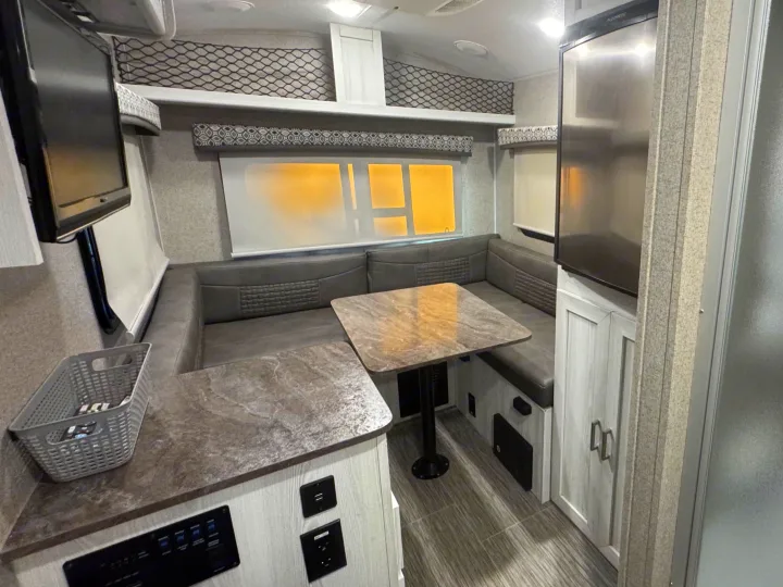 Modern RV rental dinette: U-shaped seating, a table, wall-mounted TV, and refrigerator, ideal for comfy travels.. Forest River Flagstaff E-Pro 2019