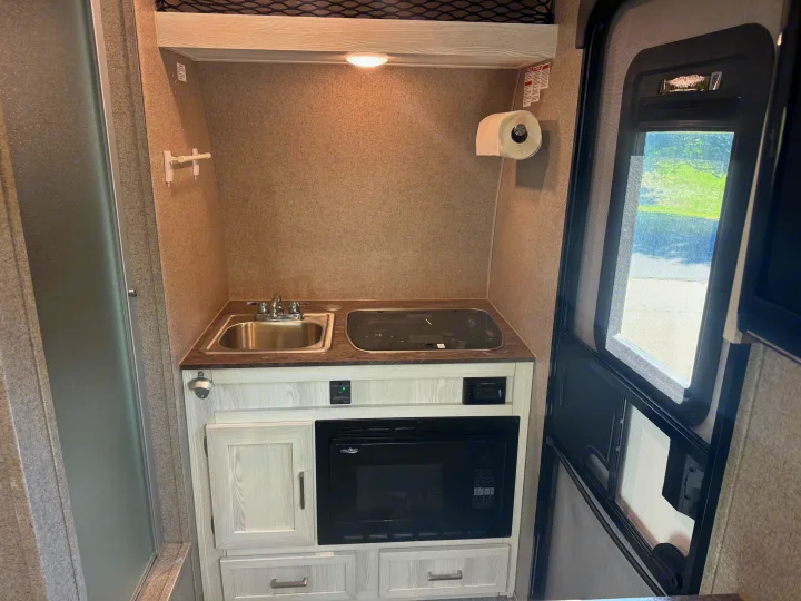 RV rental kitchen showing sink, stove, microwave, cabinets, a shower stall, and an exterior door view.. Forest River Flagstaff E-Pro 2019