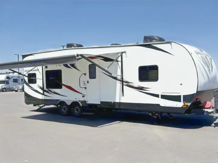 This white RV rental, with an extended awning and black/red graphics, is parked on asphalt under a clear blue sky.. Forest River Shockwave 2018