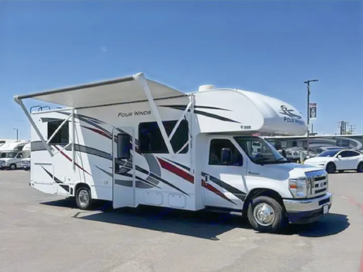 White Four Winds RV rental with an extended awning, parked outdoors under a clear blue sky, ready for adventure.. Thor Four Winds 2024