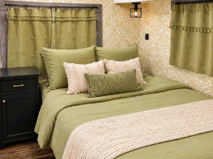 Cozy sage green bedroom in an RV rental, featuring quilted bedding, textured pillows, and leaf-patterned walls.. Coachman Mirada 2011