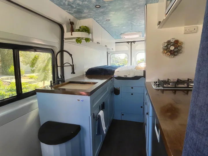 Bright RV rental interior featuring a functional kitchen, cozy bed, and custom blue cabinetry with a unique ceiling.. Dodge Ram Promaster 2500 2014