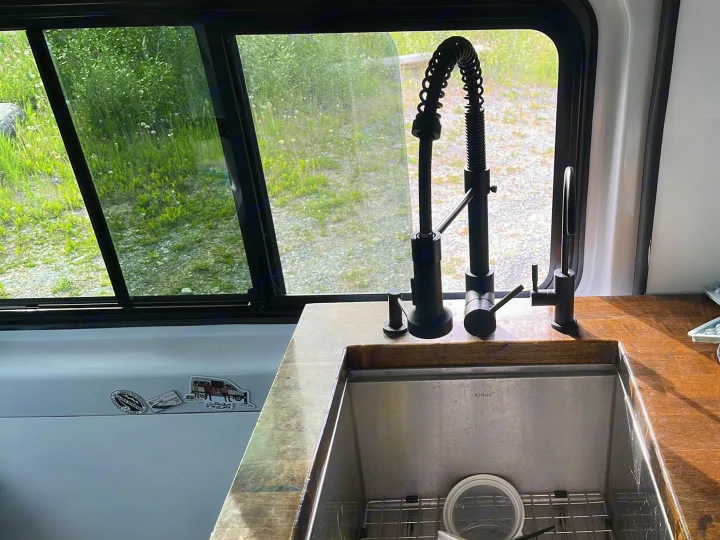 RV rental kitchen sink with modern black faucets, a wooden counter, and a window view of green nature.. Dodge Ram Promaster 2500 2014