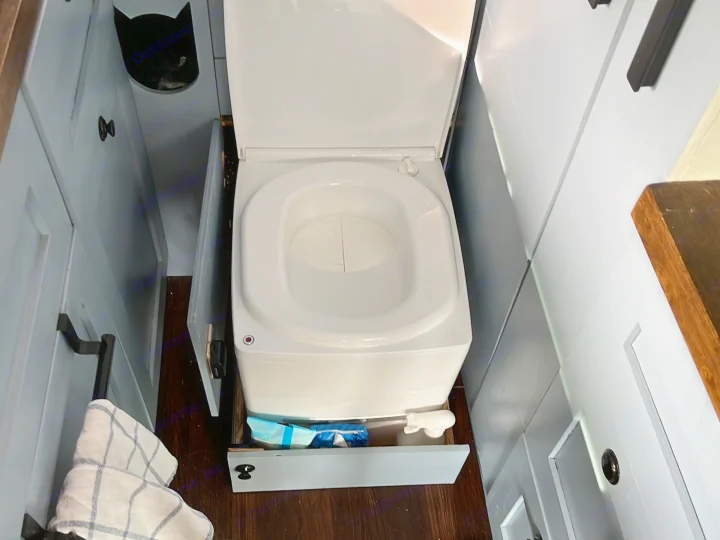 This RV rental's tiny bathroom features a compact toilet with an open lid, flanked by blue cabinets and a storage drawer below.. Dodge Ram Promaster 2500 2014