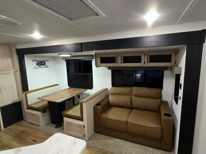 RV rental interior: dinette, cozy sofa with cup holders, and overhead cabinets. "Life's an Adventure" decal visible.. Forest River Puma 32bhqs 2027